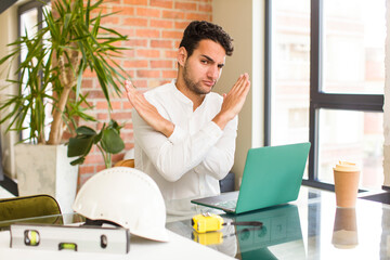 Poster - young hispanic man looking annoyed and sick of your attitude, saying enough! hands crossed up front, telling you to stop. architect concept