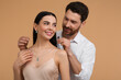 © New Africa - Man putting elegant necklace on beautiful woman against beige background