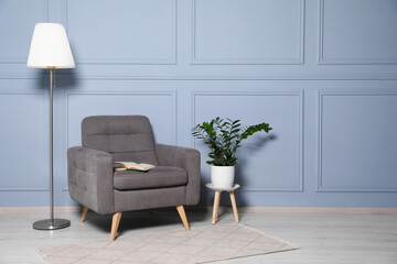 Poster - Cosy armchair, floor lamp and potted plant near light grey wall in room, space for text. Interior design