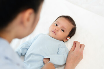 mother using cotton bud to cleaning ear of newborn baby on bed