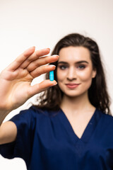 Wall Mural - Pointing at pills. Portrait of young woman, doctor, therapeutic or medical advisor wearing face mask and blue uniform isolated on white background. Concept of healthcare and medicine