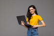 © F8  \ Suport Ukraine - Happy young woman holding laptop and looking at camera isolated over gray background