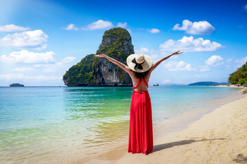 Wall Mural - A happy tourist woman in a red dress stands at the beautiful Phra Nang beach at Krabi, Thailand, during her tropical holidays