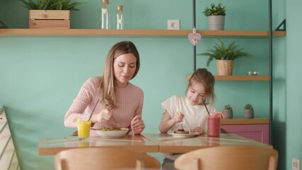 Wall Mural - Mother and daughter having good time during breakfast with fresh squeezed juices in the cafe