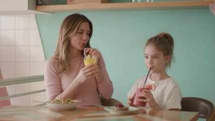 Wall Mural - Mother and daughter having good time during breakfast with fresh squeezed juices in the cafe