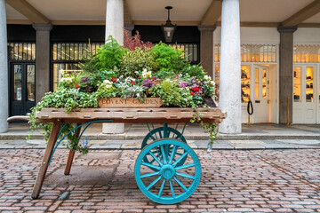 old fashioned wooden barrow with boxes of flowers, outside the stores of the world famous covent gar