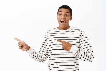 Wall Mural - Handsome smiling african american man pointing finger left, showing advertisement, promo offer, standing over white background