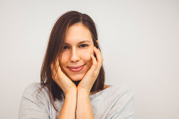 Wall Mural - Portrait of young woman holding hands on her face with a sbtle smile looking at the camera on white background 