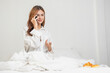 © PHAISITSAWAN - Woman in white nightgown waking up on weekend morning resting and relaxing playing with laptop mobile phone Eating bread and drinking tea in glass inside white bedroom.  Morning vacation concept.