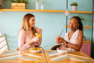 young black and caucasian woman having good time, drinking fresh juices and having healthy breakfast