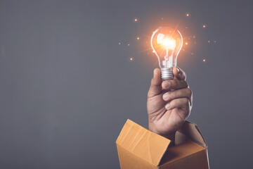 Creative new design thinking for work, Hand holding light bulb and old cardboard box on dark background, hand pops out of old cardboard box. Can use for reuse and recycle concept.