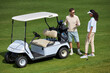 Full length portrait of elegant sporty couple standing by golf cart on green field and chatting in sunlight