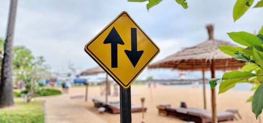 Two-way traffic warning sign. Yellow square traffic sign with black arrow symbol pointing in opposite direction. Mounted on black steel pole. Traffic signs indicate people or car can walk in opposite 