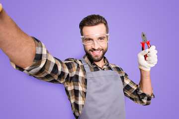 Wall Mural - Self portrait of joyful cheerful man with stubble shooting selfie on front camera, showing pliers in arm, having fun, leisure, video-call, isolated on grey background