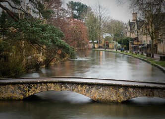 Poster - Long exposure of the river through Bourton on the Water with trees in The Cotswolds in winter