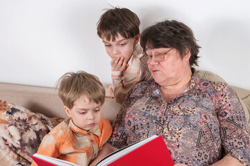 A grandmother reads an interesting book with a red cover to her grandchildren.