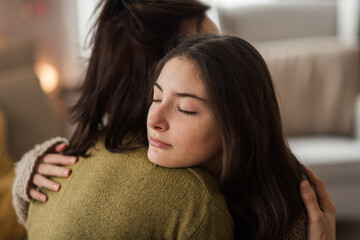 Teenage girl hugging her mother at home.