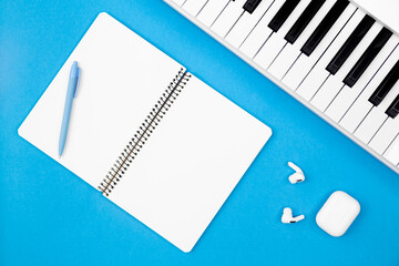 Wall Mural - Blank notebook and piano on blue background, top view, concept of musical creativity and education, white synthesizer, flat lay.