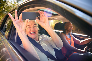 Wall Mural - Passenger Taking Selfie On Mobile Phone As Two Senior Female Friends Enjoy Day Trip Out In Car