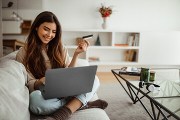 Smiling millennial mixed race woman shopaholic typing on laptop, using credit card, enjoy online shopping