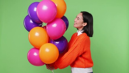 Wall Mural - Happy excited young woman of Asian ethnicity 20s wear orange sweater celebrate dance birthday holiday party hold in hand bunch of colorful air balloons isolated on plain pastel light green background