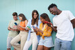 © CarlosBarquero - Young smiling multicultural group of friends using cell phones. Students leaning against a blue wall outside. Cheerful people gathered together looking at and typing on their mobiles.