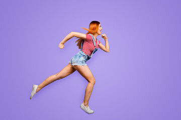 Sticker - Full-size portrait of running sporty girl in a striped T-shirt and overalls who looks in front of her isolated on bright blue background