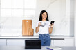 © F8  \ Suport Ukraine - Young woman using smartphone leaning at kitchen table with coffee mug and organizer in a modern home. Smiling woman reading phone message.