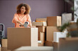 © Seventyfour - Young woman with curly hair packing cardboard boxes with adhesive tape during relocation