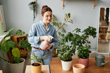 Portrait of smiling young woman watering plants indoors and caring for home greenery, copy space