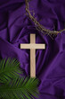 Wood cross, partial crown of thorns and palm leaves on a dark purple fabric background with copy space