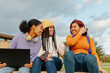 © Alberto - multiracial group of three teenage girls with unretouched skin chatting happily sitting on a bench outside the university campus. Young people using wireless technology.