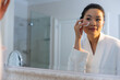 © Wavebreak Media - Happy asian woman wearing bathrobe looking in bathroom mirror cleansing face with cotton pad