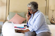 © Wavebreak Media - Focused african american senior businesswoman talking over mobile phone and using laptop on bed