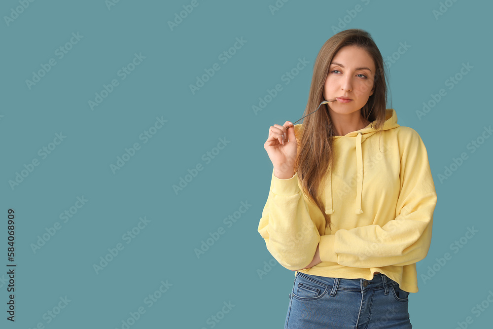 Thoughtful young woman with spoon on blue background