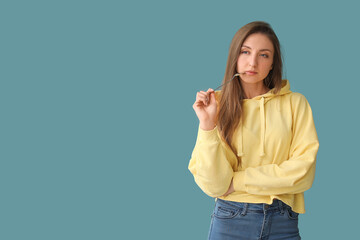 Thoughtful young woman with spoon on blue background