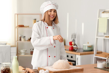 Canvas Print - Female baker sprinkling dough with flour at table in kitchen