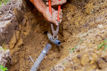 Man is working with pipes in ground while installing an underground sprinkler system to water garden on yard