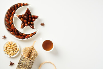 Ramadan Kareem concept. Crescent and star plate with dried dates, arabic lantern, nuts, rosary breads on white backgroud.