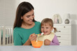 © New Africa - Mother feeding her cute little child with yogurt at white table in room