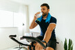 © kleberpicui - Man with water bottle working out on exercise bike at home