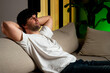 © Grustock - Handsome man sitting on a sofa in a stylish apartment. Feeling relieved after work, the man throws his hands behind his head and smiles