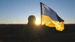 Ukrainian army woman stands to the peak of hill with waving blue-yellow banner at sunset. Young female soldier in camouflage uniform lifting flag of Ukraine. Resistance to russian invasion concept