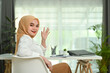 © Prathankarnpap - Positive asian Muslim woman worker in hijab waving hand at camera, greeting someone while sitting in modern office