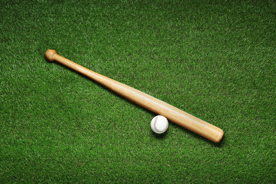 Wall Mural - Wooden baseball bat and ball on green grass, flat lay. Sports equipment