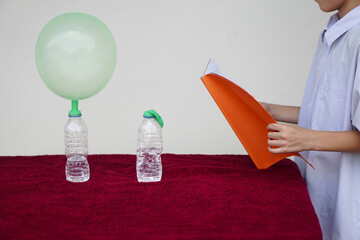 Closeup student study science experiment about reaction of chemical in bottles and balloons. Read  the result of experiment in book. Concept, science subject activity, education. Learning by doing