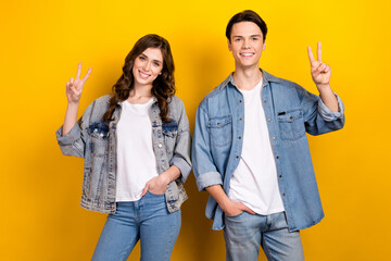 Wall Mural - Portrait of two positive satisfied people hand fingers demonstrate v-sign isolated on yellow color background