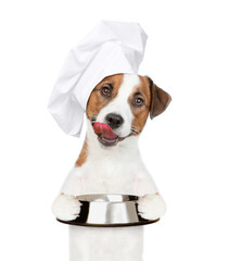 Poster - Licking lips Jack russell terrier puppy wearing a chef's hat holds empty bowl. isolated on white background