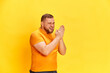 Portrait of one sneering man with smiling face standing and rubbing hands over yellow background. Close up