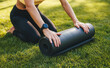 Body part of a woman in sport costume sitting and rolling up the yoga mat. Yoga and pilates concept. People body fit healthy. Sitting woman outdoors. Fitness
